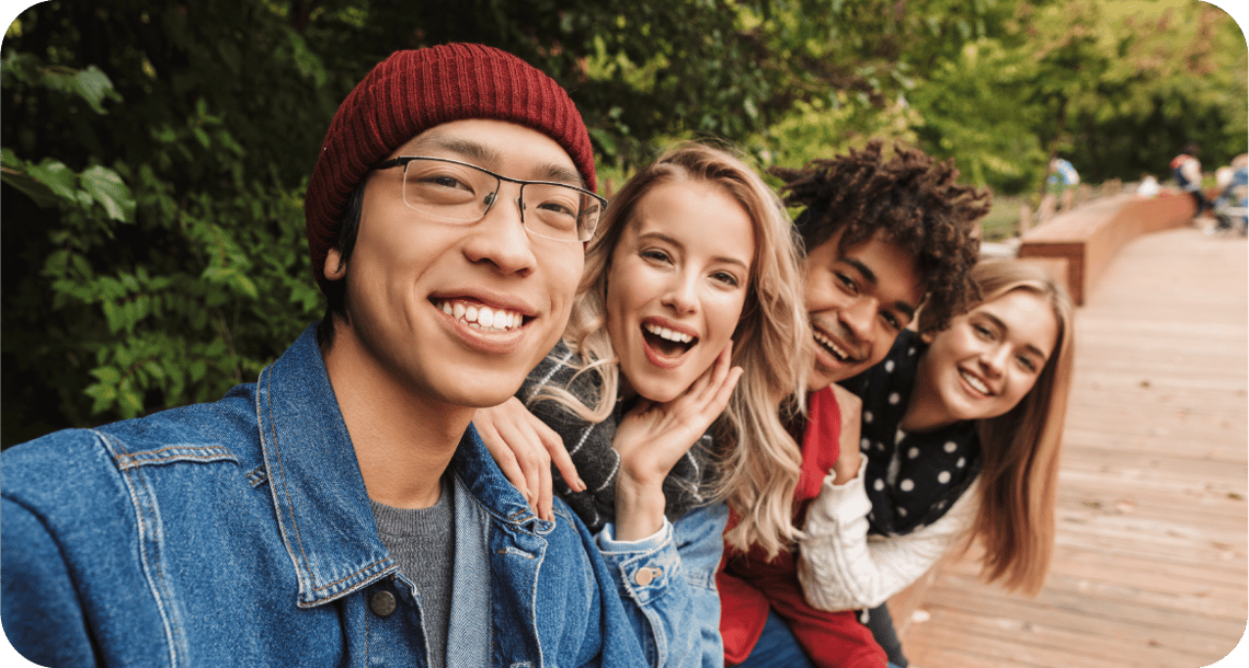 Group of smiling young people taking a selfie outdoors. 