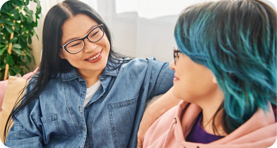 An adult or caregiver smiling at a young person while on a couch. 
