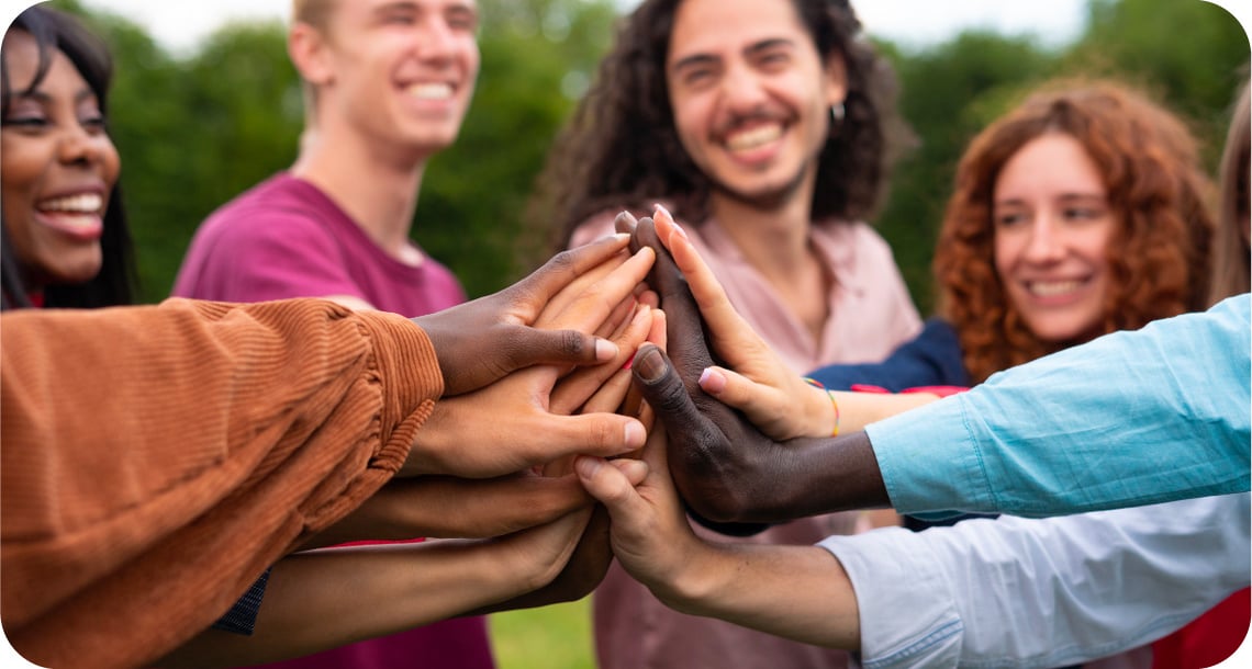 Happy young people outdoors putting their hands in the center of the group for togetherness. 