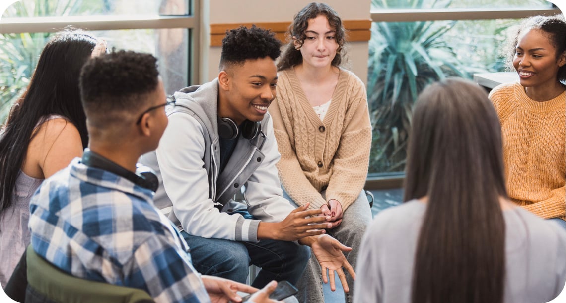  Young people sitting in a circle while happily talking in a classroom.  